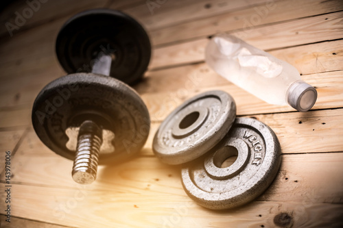 Dumbbells , weight plates and bottle of water on wooden background for bodybuilder. Concept for sport player or workout. gym of accessories for fitness