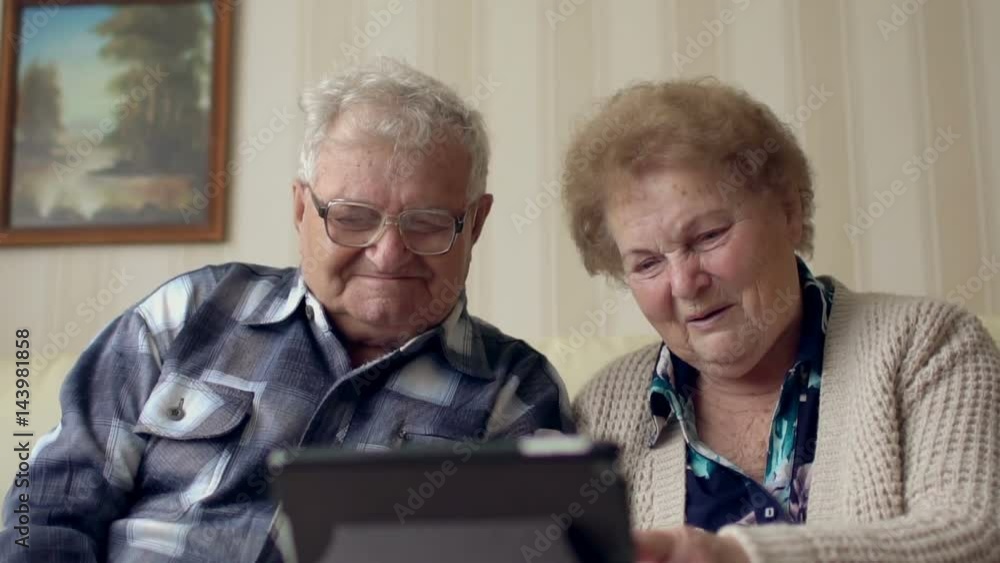 Senior couple in sofa using electronic tab. A cheerful senior couple having a video chat on a digital tablet. Senior couple in sofa using electronic tab. A cheerful senior couple having a video chat on a digital tablet.