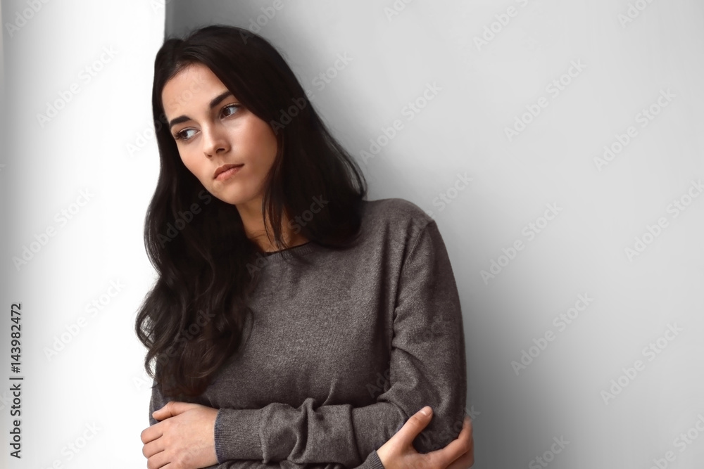 Depressed young woman standing near wall at home Depressed young woman standing near wall at home