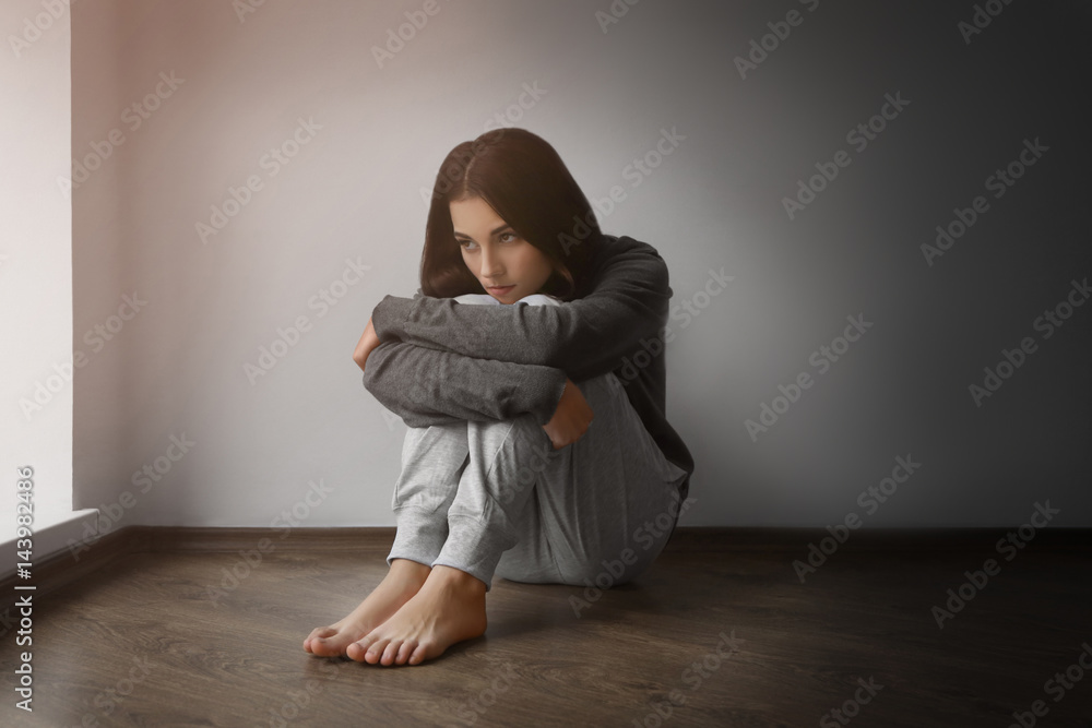 Depressed young woman sitting on floor in empty room Depressed young woman sitting on floor in empty room
