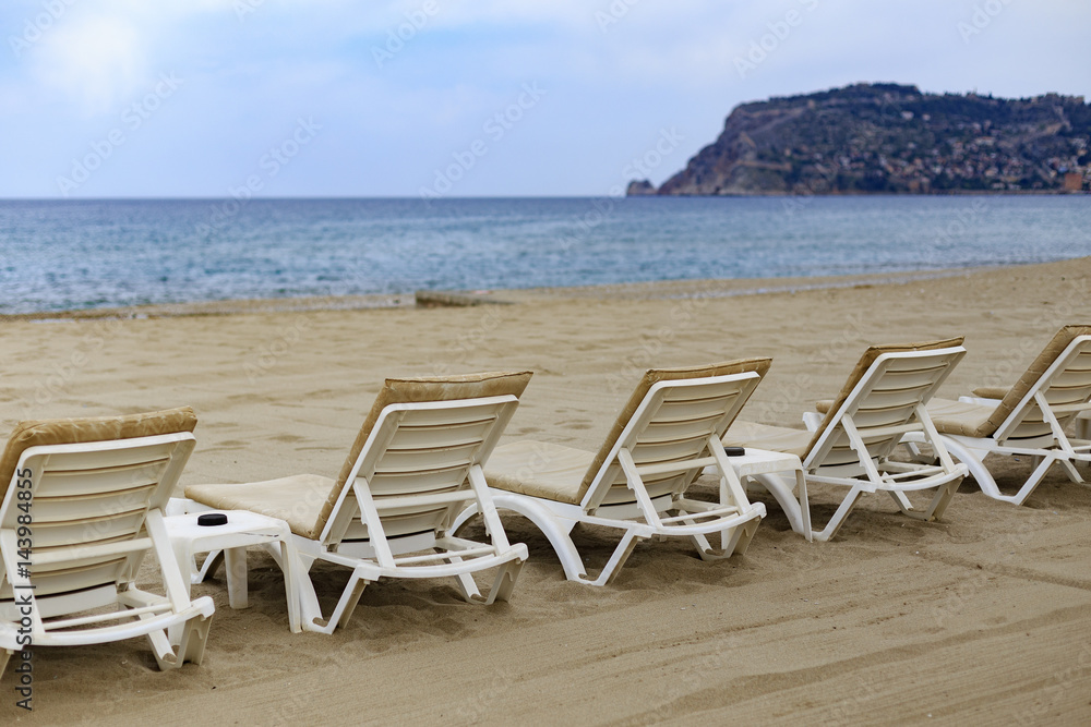 Backview of white sunbeds at sandy beach