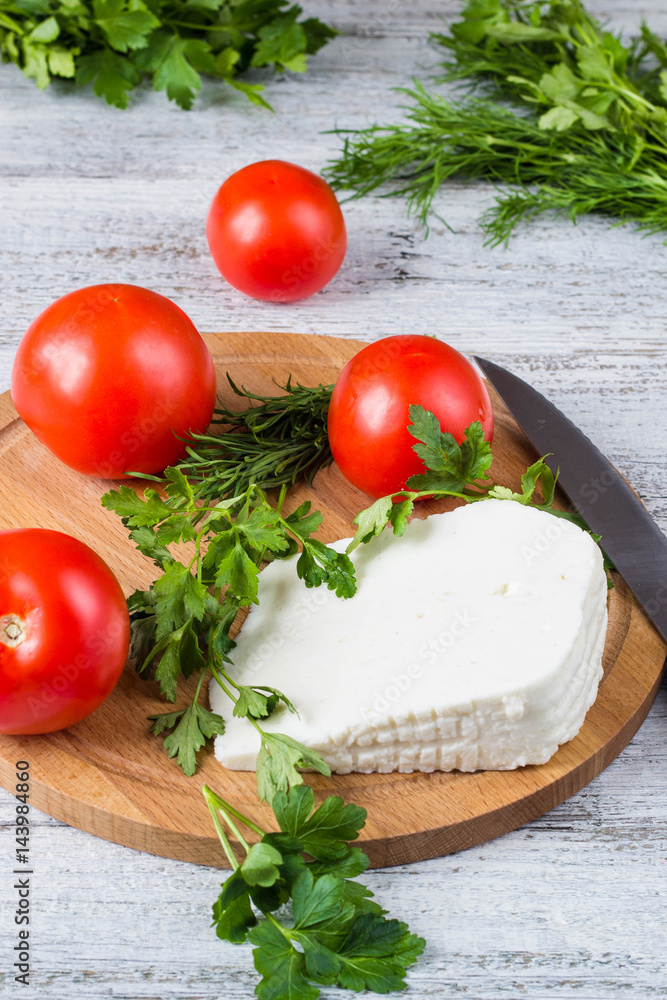 White cheese, knife, parsley, tomatoes on a wooden boards background White cheese, knife, parsley, tomatoes on a wooden boards background
