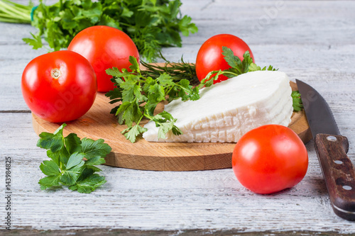 White cheese, knife, parsley, tomatoes on a wooden boards background