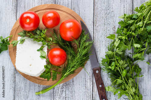 White cheese, knife, parsley, tomatoes on a wooden boards background