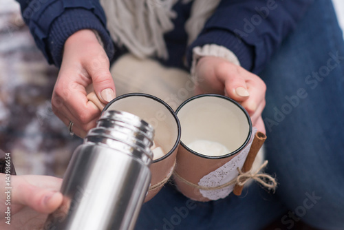Young couple pours hot drink out of thermos, winter picnic