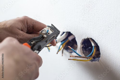 Pliers peeling copper wires. Сloseup on electrician hands, wall sockets in the background