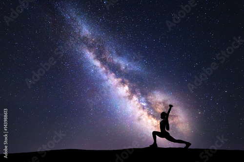 Milky Way with silhouette of a standing woman practicing yoga on the mountain. Beautiful landscape with meditating girl against night starry sky with milky way. Amazing galaxy. Universe. Fitness