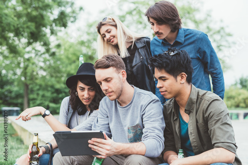 Group of friends multiethnic millennials outdoor using tablet - technology, social network, togetherness concept