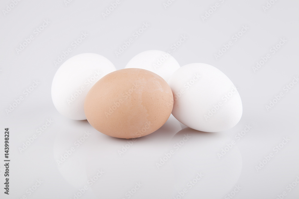 Three white eggs and one brown egg on a white surface. Isolated on white background. Three white eggs and one brown egg on a white surface. Isolated on white background.