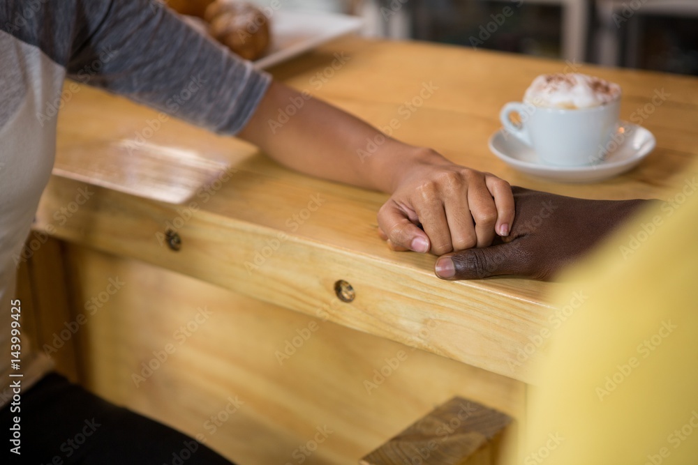 Multi ethnic couple holding hands in coffee house Multi ethnic couple holding hands in coffee house