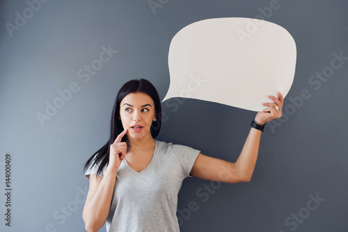 Fotografía Young woman posing with a speech bubble against a grey background