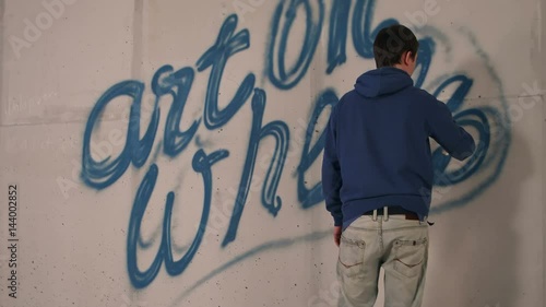 Young man drawing graffiti on a wall with a spray can