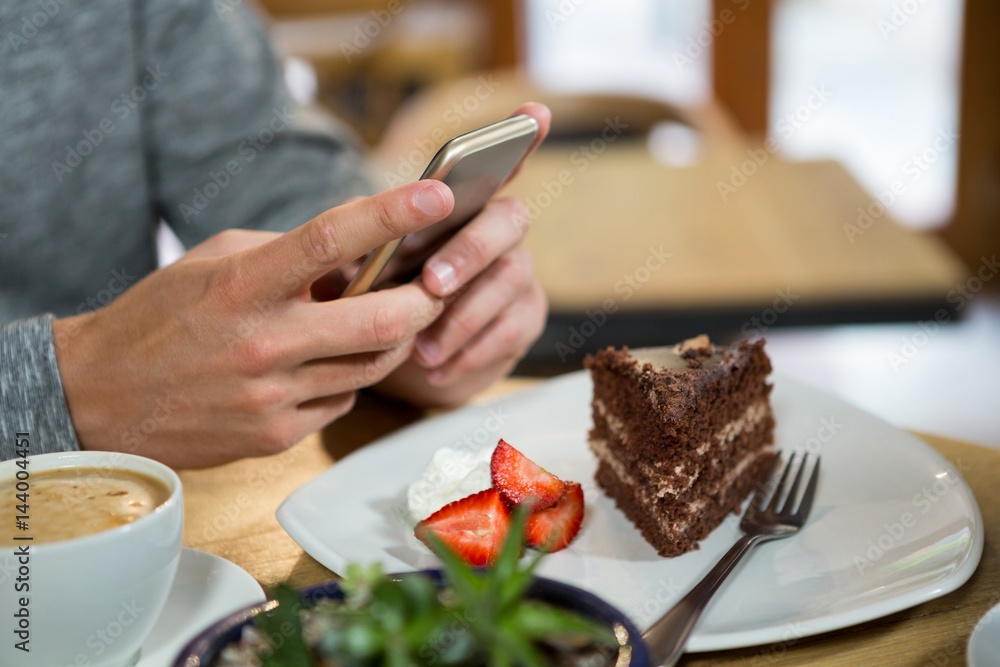 Man using mobile phone with coffee and dessert on table in cafe