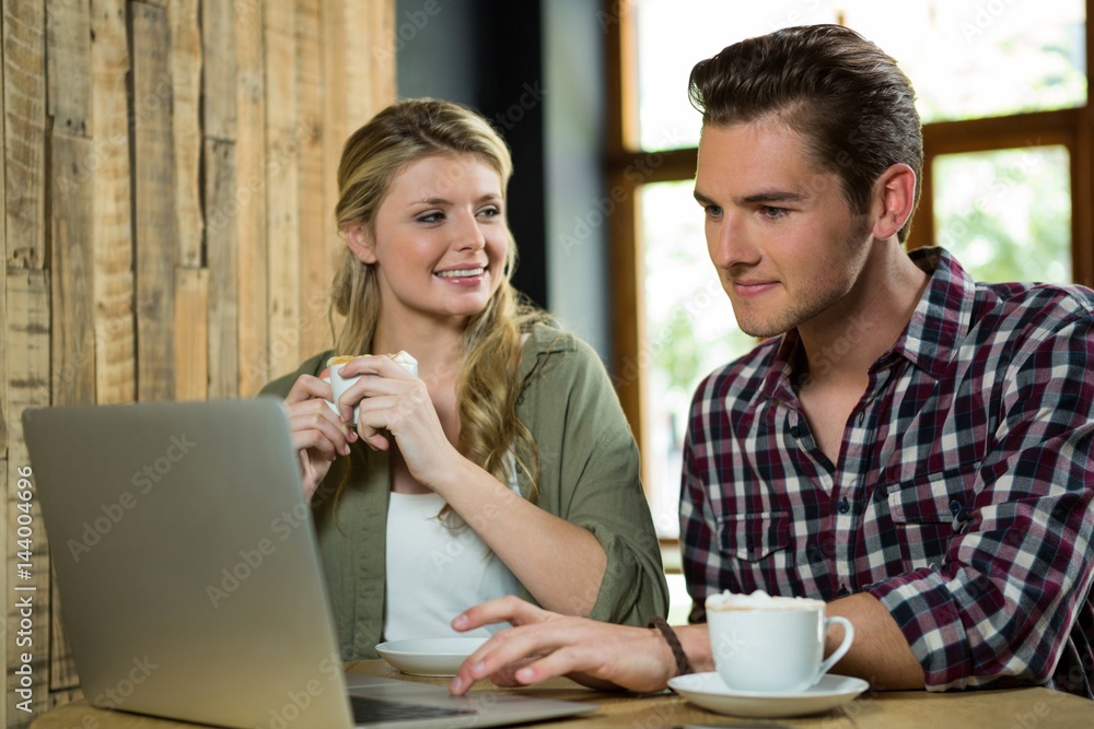 Woman looking at man using laptop in coffee shop Woman looking at man using laptop in coffee shop