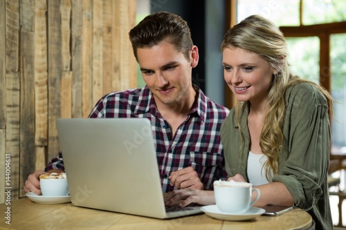 Smiling couple using laptop at table in coffee shop