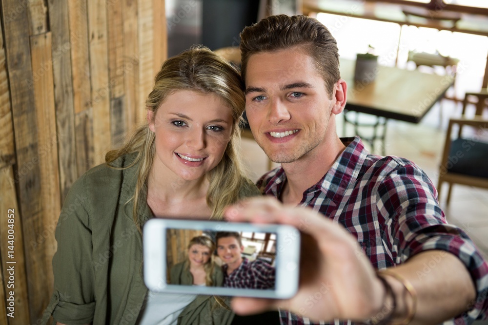Smiling couple taking selfie with mobile phone in cafeteria Smiling couple taking selfie with mobile phone in cafeteria