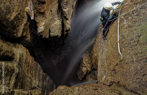 Explore the breathtaking Mayei Cave in Ecuadorian Amazonia with a speleologist inside a deep waterfall entrance shaft,capturing the blurred motion of adventure. photo