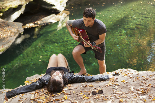 Young man serenading his girlfriend by a stream photo