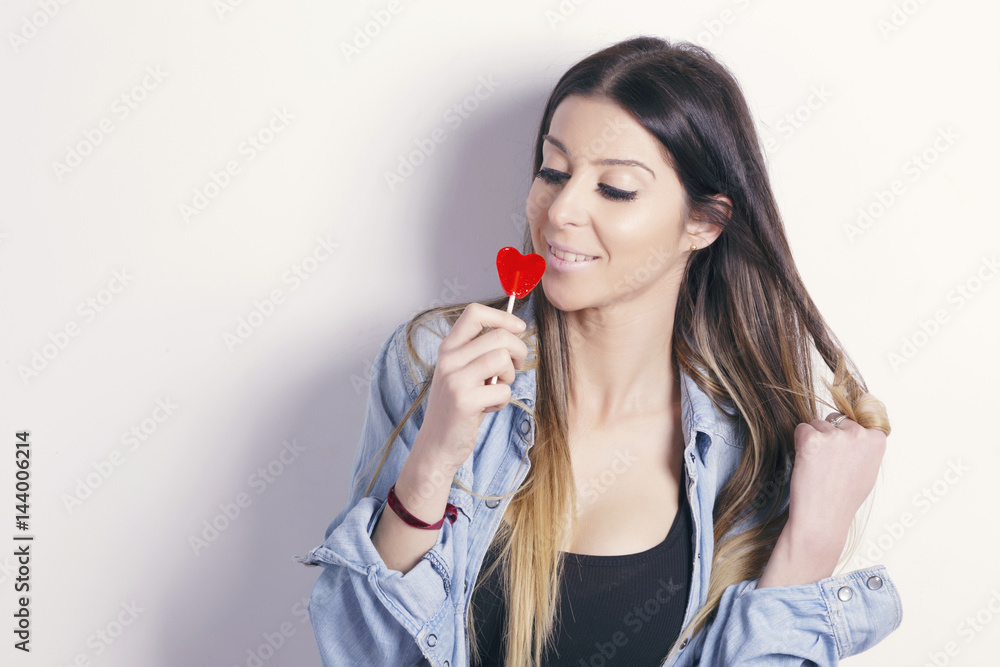 Young woman with a heart shaped lollipop, having fun with it, over a white background. Young woman with a heart shaped lollipop, having fun with it, over a white background.