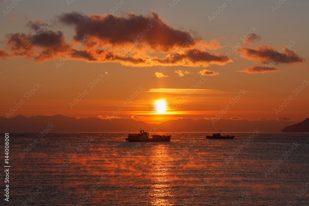 Two ships floating on background of red sunset