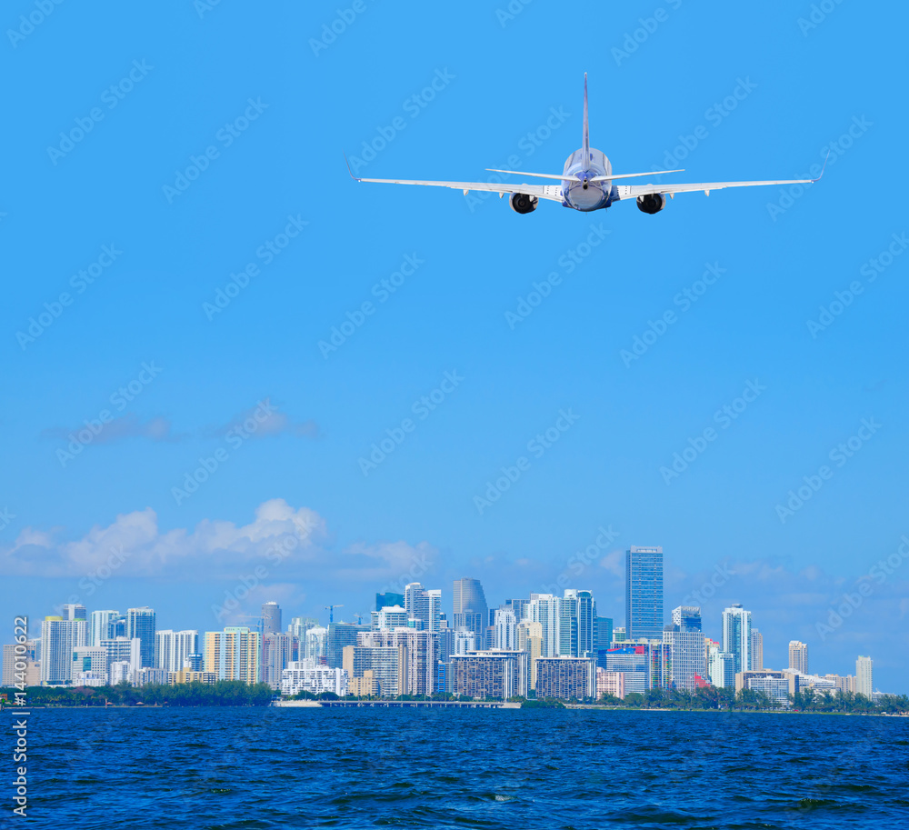 Miami, Florida, skyline viewed from Biscayne Bay with a commercial passenger jet airliner plane flying arriving or departing the International Airport. Miami, Florida, skyline viewed from Biscayne Bay with a commercial passenger jet airliner plane flying arriving or departing the International Airport.