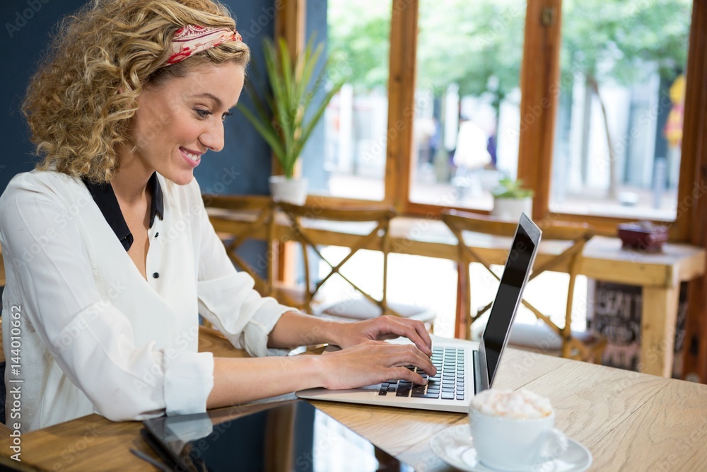 Fotografie Smiling woman using laptop at table in cafeteria