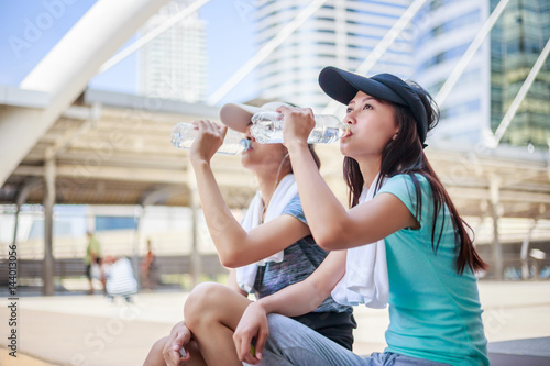 Beautiful young asian woman drinking water after training in city