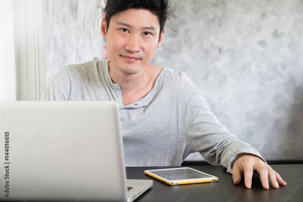 Happy casual young man using laptop on the desk and looking at the camera. Happy casual young man using laptop on the desk and looking at the camera.