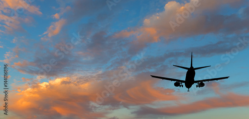 Silhouette of landing airplane, background of colorful clouds