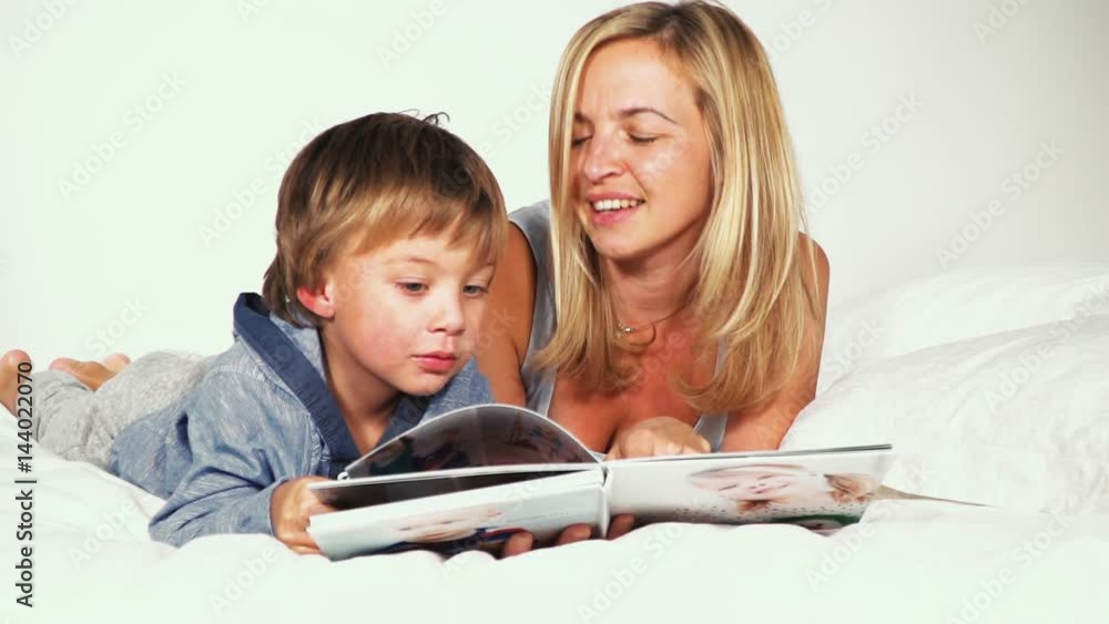 mutter und sohn liegen im bett und schauen gemeinsam ein familien fotobuch an mutter und sohn liegen im bett und schauen gemeinsam ein familien fotobuch an