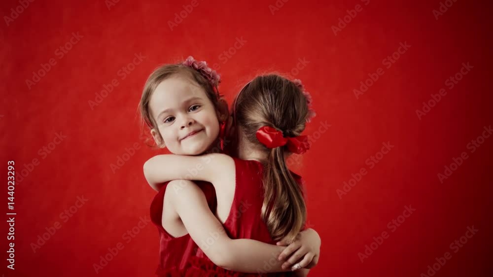 Two little girls hugging on a red background Two little girls hugging on a red background