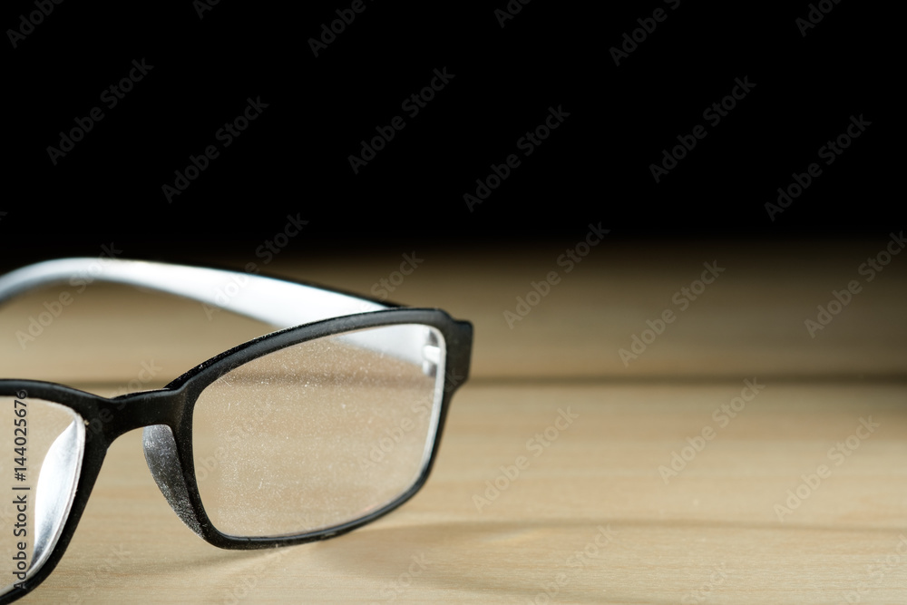 black glasses with long shadow dirty by dust put on wooden table and black background black glasses with long shadow dirty by dust put on wooden table and black background