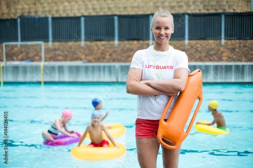 Female lifeguard standing with rescue can at poolside photo