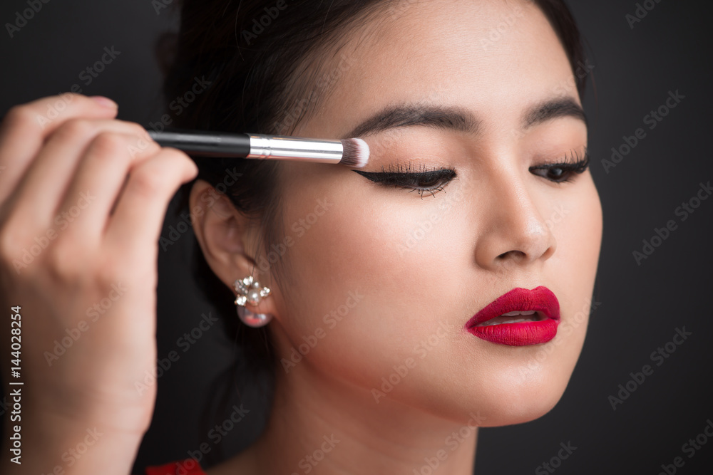 Close up of hand of asian woman applying eyeshadow on female eyelid. Close up of hand of asian woman applying eyeshadow on female eyelid.