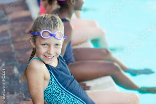 Happy girl sitting with friends at poolside