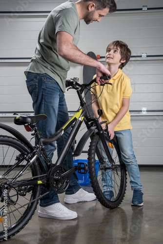Smiling father and son standing with bicycle and looking at each other