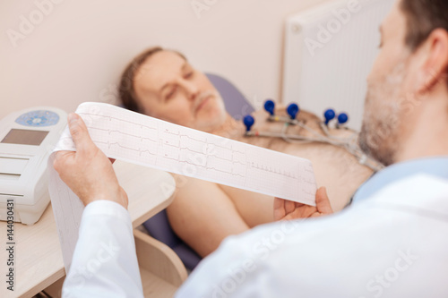 Excellent trained cardiologist carefully studying patients cardiogram photo