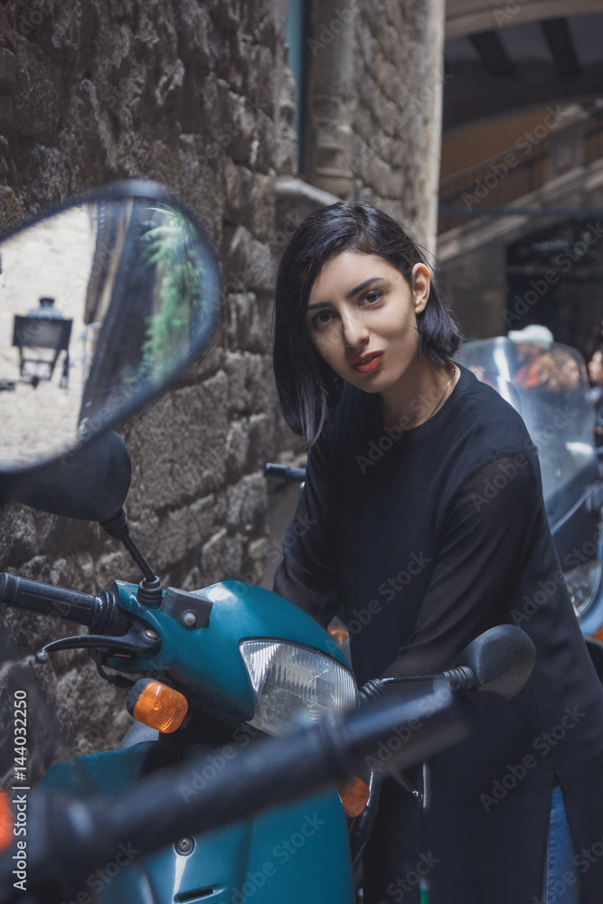 Young beautiful woman posing near scooter in old town