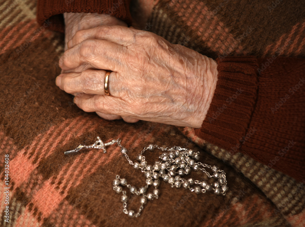 Close up of old woman praying with silver rosary with cross