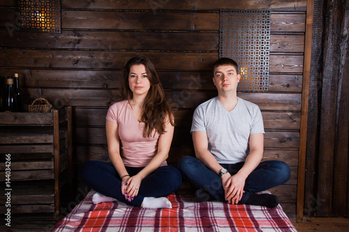 Young couple sitting crosslegs on plaid near dark wooden wall. Countryside style photo