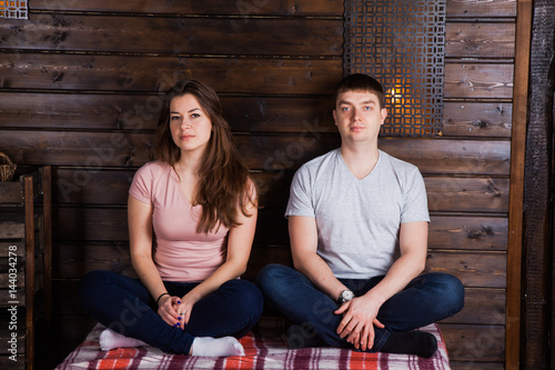 Young couple sitting crosslegs on plaid near dark wooden wall. Countryside style photo