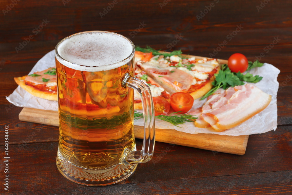Mug of light beer and pizza with smoked meat are on dark wooden background. Mug of light beer and pizza with smoked meat are on dark wooden background.