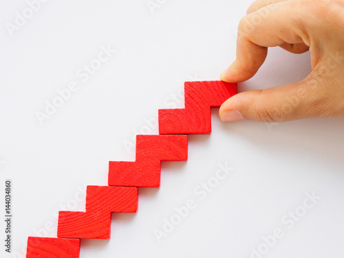 Concept of building success foundation. Women hand put red puzzle wooden blocks in the shape of a staircase