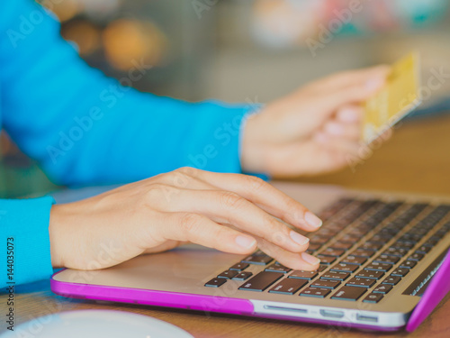 Pretty Young womans hands holding a credit card and using tablet, smartphone and laptop computer for online shopping. Online payment. Female working on smart phone laptop in a cafe.