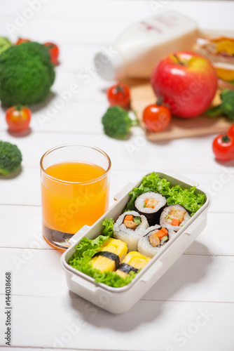 Orange juice and bento box with different food, fresh veggies and fruits