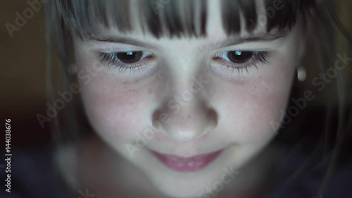 Night shot of kid's girl face browsing tablet pc with light reflection on it