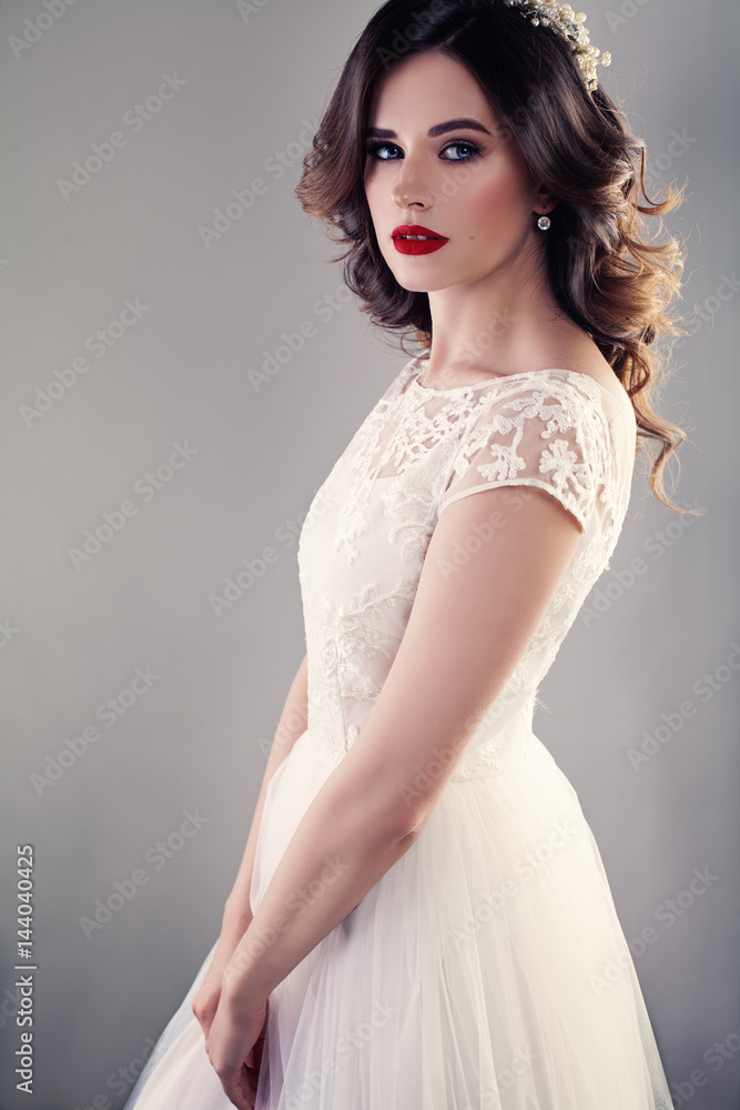 Fashionable gown, beautiful blonde model, bride hairstyle and makeup  concept - young lovely girl in white wedding festive dress, standing  indoors on light background, romantic slender woman posing. Stock Photo by  ©melnikofd@yandex.ru