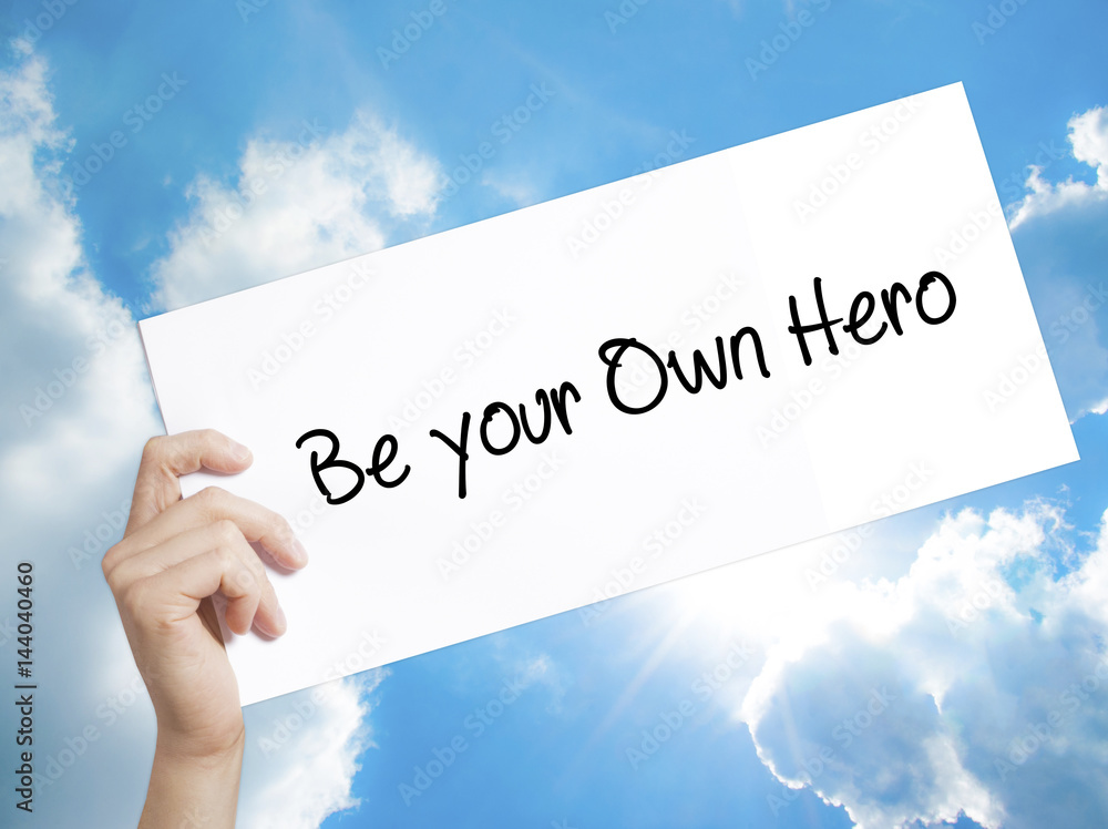Be your Own Hero Sign on white paper. Man Hand Holding Paper with text. Isolated on sky background Be your Own Hero Sign on white paper. Man Hand Holding Paper with text. Isolated on sky background