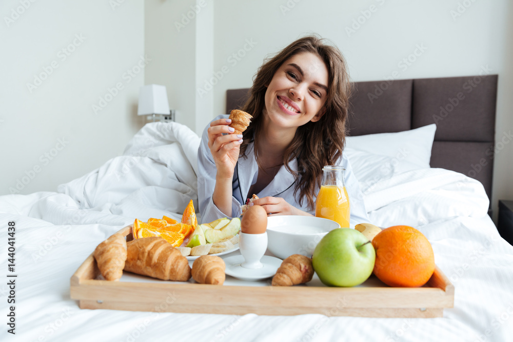 Portrait of a pretty happy woman having breakfast in bed