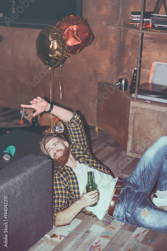 drunk bearded man lying on floor in messy room after party